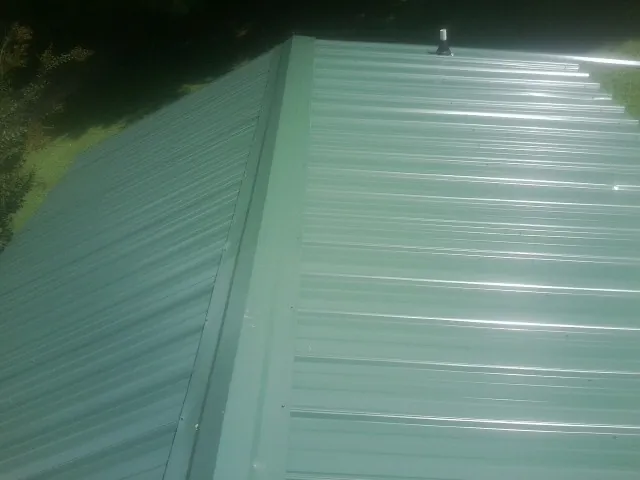 New green metal panels meeting at the ridge of a roof — Flat Roof Repair work by our crew in Ridgeville