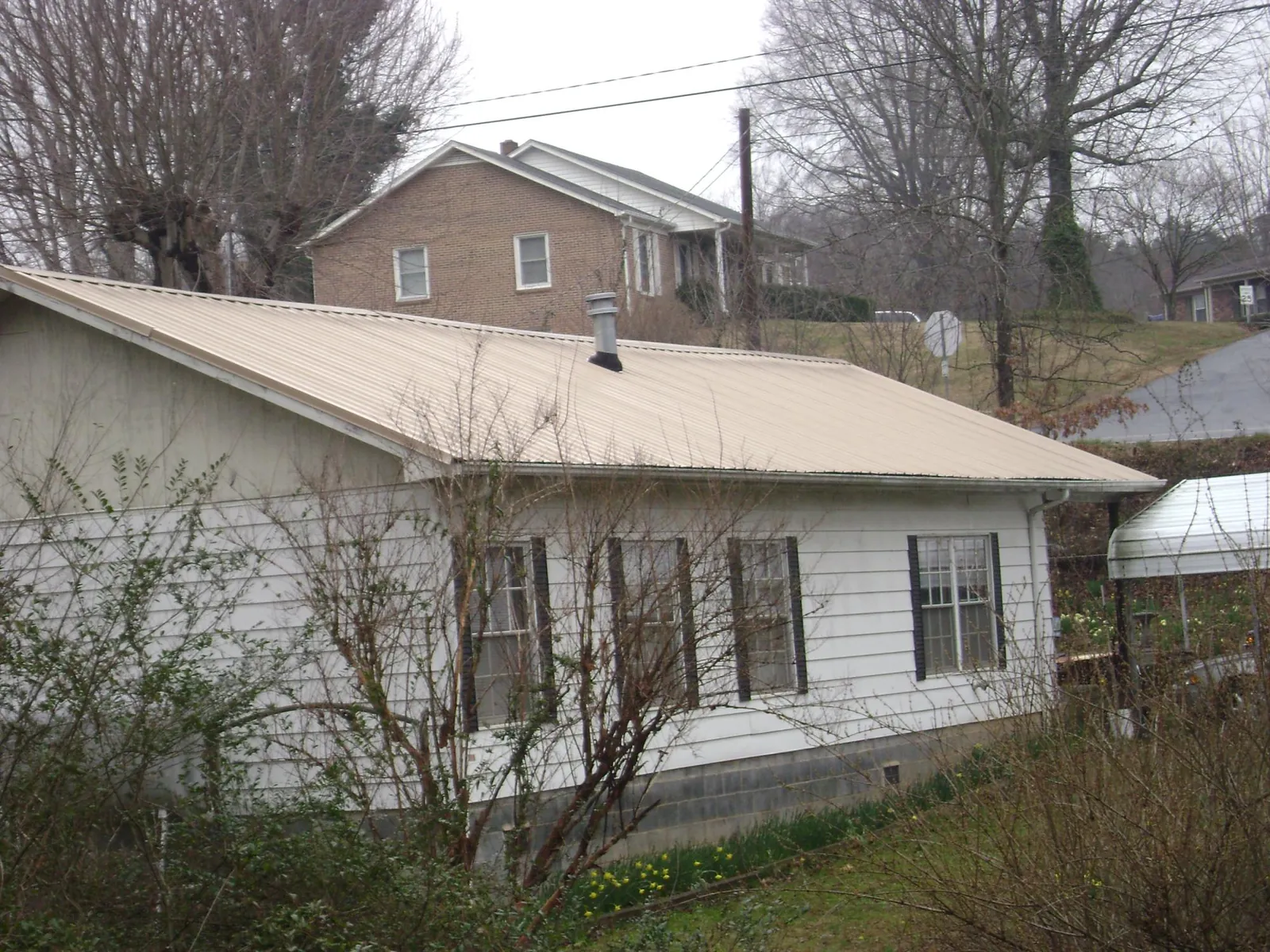 Tan metal roof on a white sided house set into a hillside — Commercial Roofing by Roofing Brothers in Ridgeville